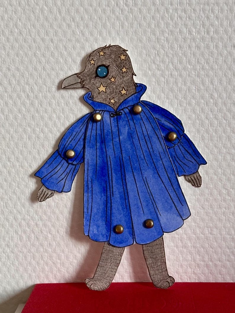 May include: A whimsical paper cutout of a bird-like figure. The figure has a gray head adorned with gold stars and a blue eye. It wears a blue coat with gold buttons. The figure stands on a red surface.