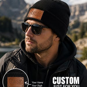 May include: A black knit beanie featuring a rectangular brown leather patch on the front. The patch is secured with four metal rivets and has the name GRAYSON embossed in the centre. The text CUSTOM JUST FOR YOU PERSONALIZED. UNIQUE. YOURS. is visible.