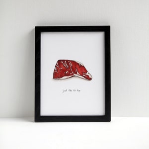 May include: A framed watercolour print showing a red and white tri-tip steak illustration. The black frame surrounds the image, which includes the text "just the tri tip" in a handwritten font.