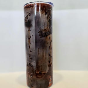 Pode incluir: Um copo de a&ccedil;o inoxid&aacute;vel com um design desgastado castanho e cinzento. O copo apresenta as palavras "Real" e "I could" numa fonte manuscrita. A parte inferior do copo tem um design de cone de tr&acirc;nsito laranja.