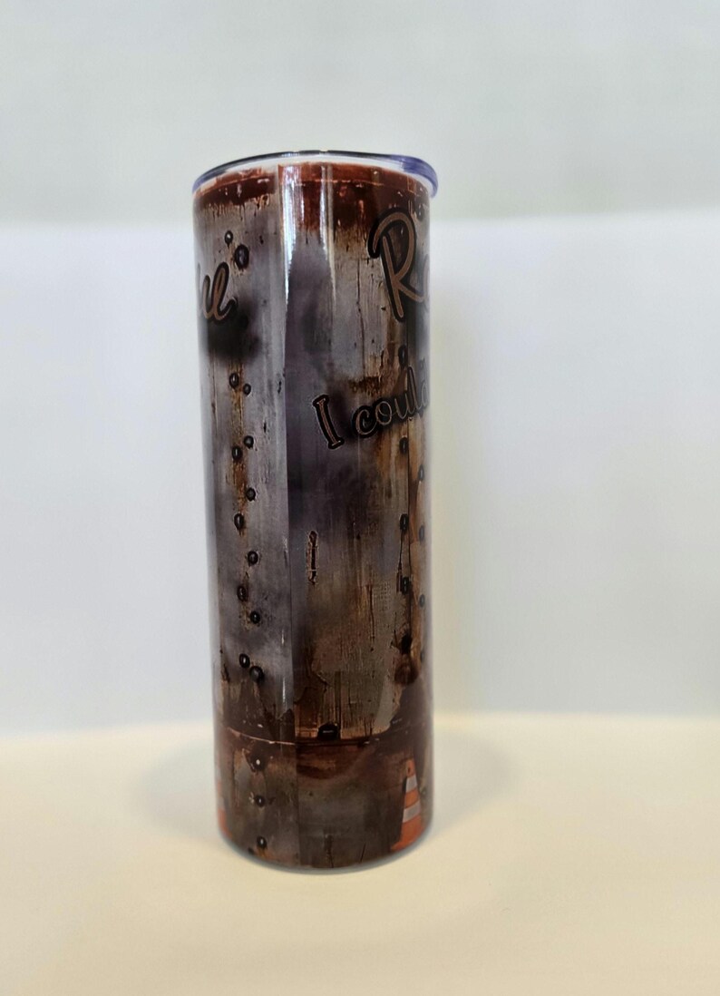 Pode incluir: Um copo de a&ccedil;o inoxid&aacute;vel com um design desgastado castanho e cinzento. O copo apresenta as palavras "Real" e "I could" numa fonte manuscrita. A parte inferior do copo tem um design de cone de tr&acirc;nsito laranja.