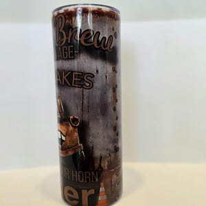 Pode incluir: Um copo de a&ccedil;o inoxid&aacute;vel com um design de metal desgastado. O copo apresenta as palavras "Brew Garage" e "Your Horn Era" em uma fonte marrom vintage. Um personagem de desenho animado e um cone de tr&acirc;nsito tamb&eacute;m s&atilde;o vis&iacute;veis.