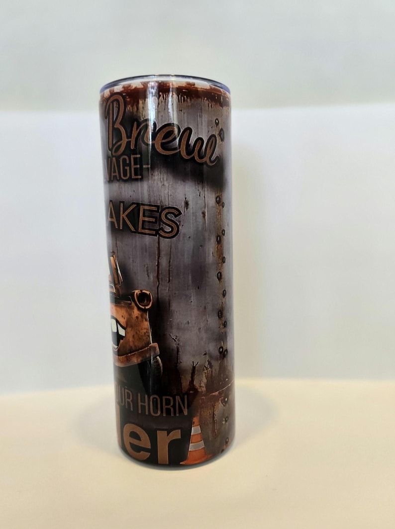 Pode incluir: Um copo de a&ccedil;o inoxid&aacute;vel com um design de metal desgastado. O copo apresenta as palavras "Brew Garage" e "Your Horn Era" em uma fonte marrom vintage. Um personagem de desenho animado e um cone de tr&acirc;nsito tamb&eacute;m s&atilde;o vis&iacute;veis.