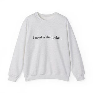 May include: A light gray sweatshirt with the phrase "i need a diet coke." printed in black. The sweatshirt has a crew neck and long sleeves, perfect for casual wear.