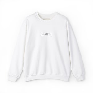 May include: White crew neck sweatshirt with the text "BORN TO YAP" in black, centered on the chest. The sweatshirt has long sleeves and a simple, minimalist design, suitable for casual wear.