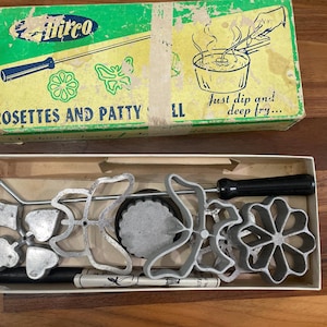 May include: Vintage Hirco Rosettes and Patty Shell set. The box is green and yellow with the words "Rosettes and Patty Shell" printed on the front. Inside the box are various metal rosette and patty shell molds with black handles.