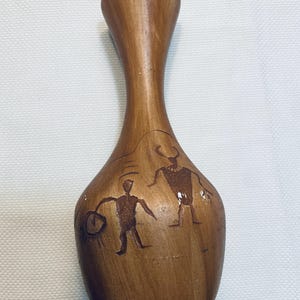 May include: A wooden vase with a narrow neck and a bulbous body. The vase is brown with etched figures of people and animals. The figures are in a dark brown color. The vase is likely handmade and has a rustic aesthetic.