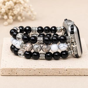 May include: Three beaded bracelets in black, white, and gray tones are attached to a silver smartwatch. The bracelets feature round beads with decorative silver spacers. The beads are made of onyx, marble, and clear quartz.