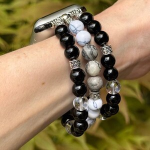 May include: A beaded Apple Watch band featuring black, white, and gray stone beads. The band includes clear and silver accent beads. The band is attached to a silver watch case.