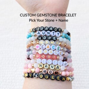 May include: A collection of custom gemstone bracelets with letter beads spelling out words such as COURAGE, AUNTY, HOPE, and MOM. The bracelets feature various coloured gemstones and gold accents. Text on the image reads: CUSTOM GEMSTONE BRACELET, Pick Your Stone + Name.