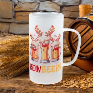 May include: A frosted glass beer mug with a white handle. The mug features a festive design of three beer glasses decorated as reindeer with the text "REINBEERS" in red and yellow.