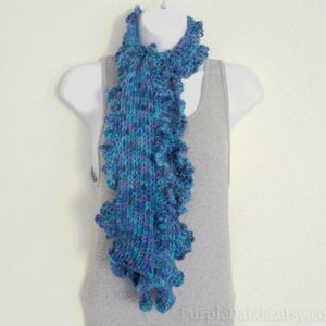 May include: A blue and purple ruffled knit scarf. The scarf is made of a soft, textured yarn and has a delicate, feminine look.