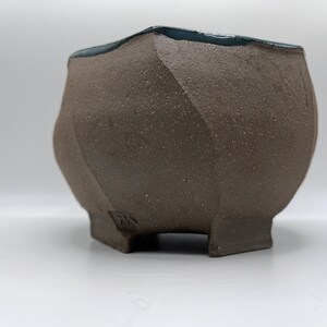 May include: A brown ceramic planter with a blue glaze on the rim. The planter has a geometric shape and four legs.