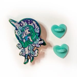 Pu&ograve; includere: Uno spillo in smalto verde e blu con una ragazza dei cartoni animati con lunghi capelli verdi, vestita con un vestito verde e che tiene una stella. Lo spillo &egrave; su uno sfondo di una galassia vorticosa. Lo spillo viene fornito con due chiusure in metallo a forma di cuore.