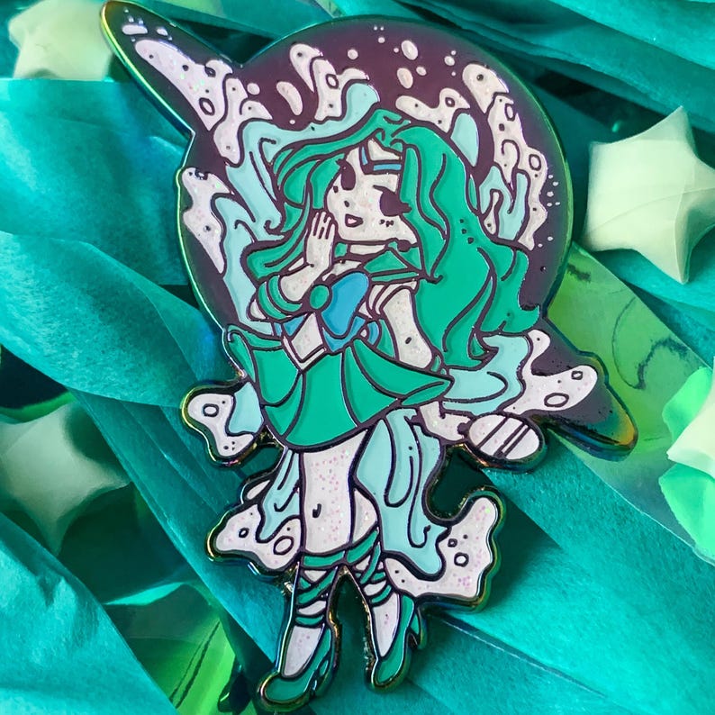 Pu&ograve; includere: Uno spillo in smalto verde e blu con un personaggio dei cartoni animati con lunghi capelli verdi, che indossa un'uniforme da marinaio verde e blu, in piedi in un vortice di acqua verde e bianca. Lo spillo ha una finitura lucida e iridescente.