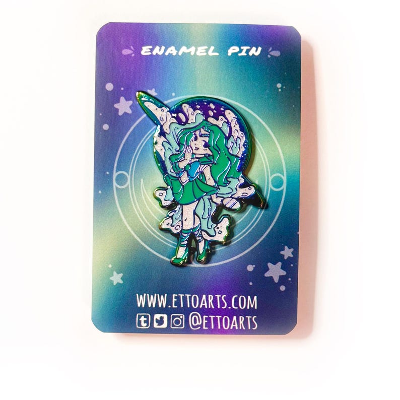 Pu&ograve; includere: Una spilla in smalto olografico con un personaggio dai capelli verdi con un vestito verde e ali bianche. Il personaggio &egrave; in piedi su una luna crescente con stelle sullo sfondo. La spilla dice "ENAMEL PIN" in alto e "WWW.ETTOARTS.COM" in basso.