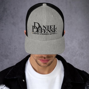Puede incluir: Una gorra de camionero gris y negra con un logotipo bordado en negro que dice "Daniel Defense" y el texto "Lighter, Stronger, Better..." en una fuente más pequeña.