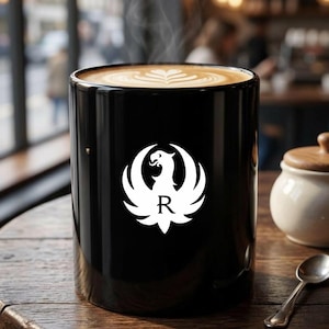Black ceramic mug featuring a white phoenix logo with letter R. Ideal gun enthusiast mug, Ruger coffee mug, firearms brand drinkware, patriotic mug, military supporter mug, veteran coffee cup, tactical mug, range day mug, unisex coffee mug, office mug, collector mug, American pride mug, shooting sports mug, gun owner gift, second amendment mug, everyday use mug, black matte mug, logo coffee cup.