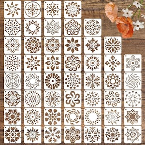 May include: A set of 48 square stencils featuring diverse geometric and floral patterns. The stencils, made from a light-coloured material, are arranged in a grid. Designs include snowflakes, mandalas, and other decorative motifs for crafts and art projects.