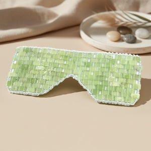 Jade Renewal Weighted Eye Mask, crafted from 100% authentic jade stone beads. Naturally cooling and calming, jade has long been cherished for its ability to reduce puffiness, soften fine lines, and restore balance. Use chilled to refresh tired eyes and soothe irritation, or warmed to relax tension and encourage circulation. More than skincare, this mask is a moment of meditation—inviting calm, clarity, and radiant renewal.