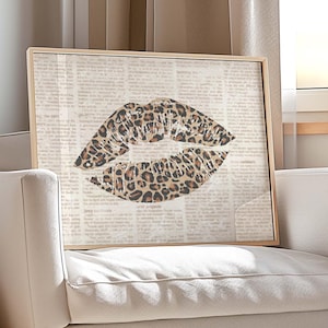 May include: A framed artwork featuring a leopard print lip design. The print is set against a neutral background, displayed on a white armchair with wooden legs. The room is illuminated by natural light.