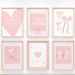 May include: Six framed pink art prints with gold frames. The prints feature a heart, bows, a martini, a playing card, and a butterfly. Text on the prints includes "this must be the place", "sweet dreams", and "How lucky are we?"