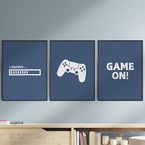 May include: Three framed prints with a gaming theme. The left print says "LOADING..." with a progress bar. The center print features a white game controller. The right print says "GAME ON!" All prints have a dark blue background.