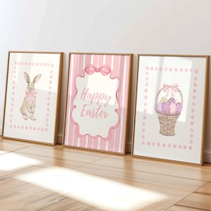 Pode incluir: Três impressões emolduradas com tema de Páscoa. As impressões apresentam um coelho com um laço rosa, o texto "Happy Easter" e uma cesta de ovos. Cada impressão tem uma borda rosa pontilhada e uma moldura dourada.