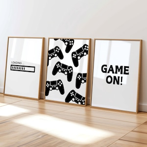 May include: Three framed art prints with a gaming theme. One print says "LOADING..." with a progress bar. Another features a pattern of black game controllers. The third print says "GAME ON!" in bold black letters.