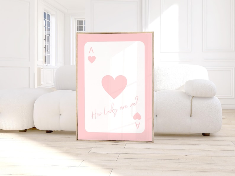 May include: A framed pink and white art print featuring a playing card design. The card is the Ace of Hearts, with a large heart in the center and the text "How lucky are we?" in a script font.
