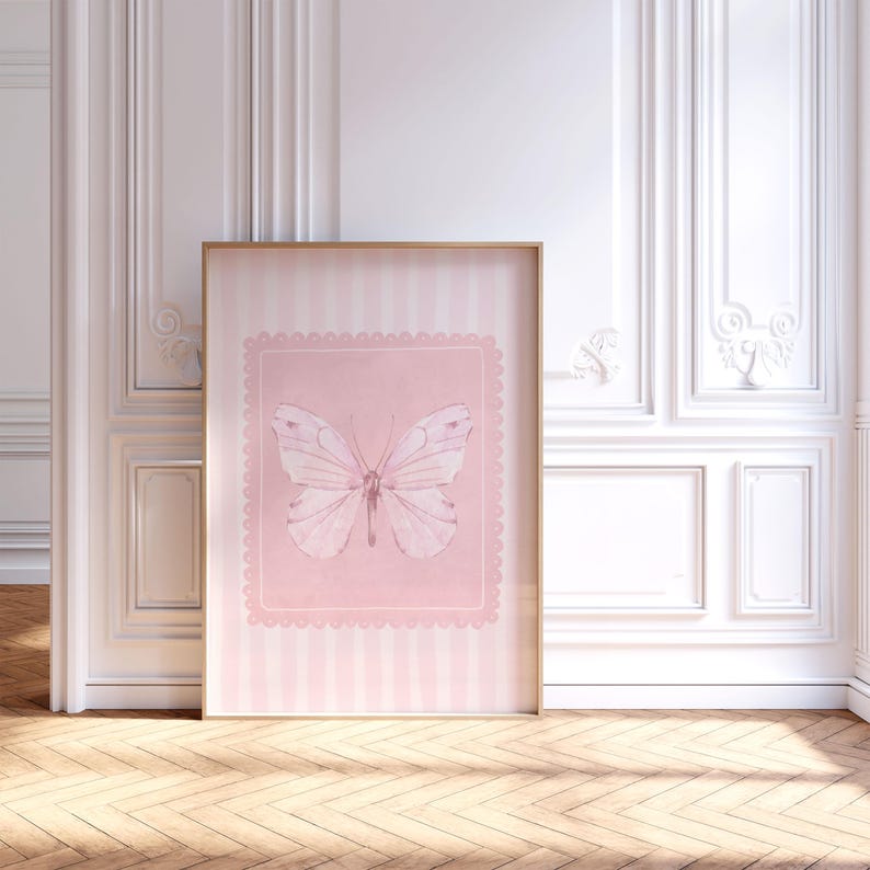 May include: A framed pink and white butterfly print. The artwork features a light pink background with a scalloped border and a watercolor-style butterfly. The frame is a light wood color, and the background has vertical stripes.