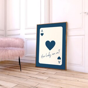 May include: A framed art print featuring a playing card design. The card is an Ace of Hearts, with the text "How lucky are we?" in a handwritten font. The print has a navy blue border and a wooden frame.