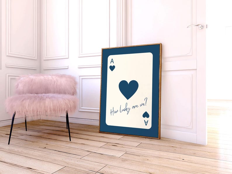 May include: A framed art print featuring a playing card design. The card is an Ace of Hearts, with the text "How lucky are we?" in a handwritten font. The print has a navy blue border and a wooden frame.