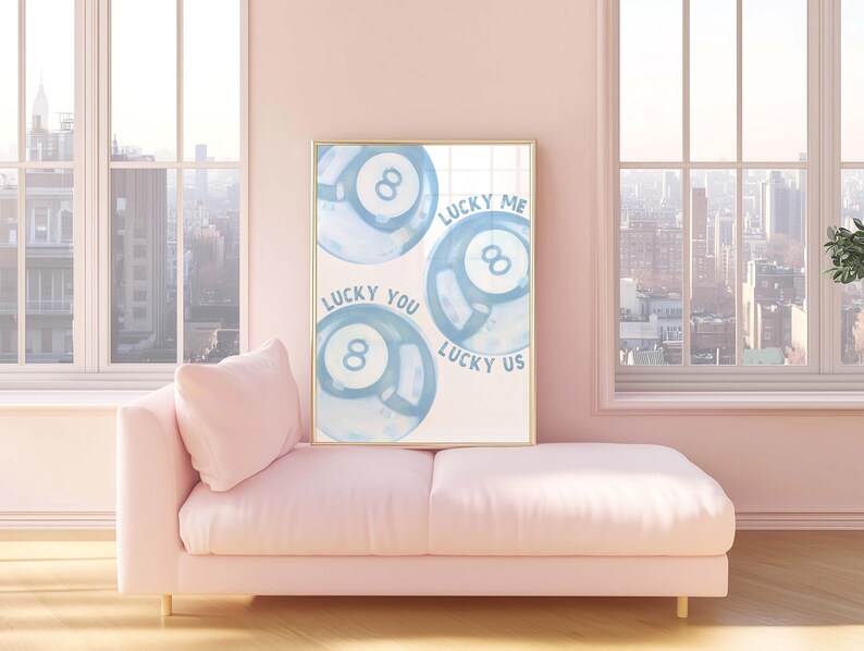 May include: A framed art print featuring three blue watercolor-style eight balls. The text on the print reads "Lucky Me," "Lucky You," and "Lucky Us." The print is displayed in a room with a pink sofa and a city view.