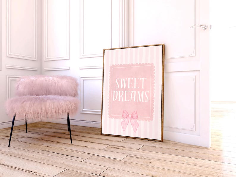 May include: A framed pink and white striped print with the words "SWEET DREAMS" and a bow illustration. A fluffy pink chair with black legs sits to the left. The room has white paneling and light wood floors.