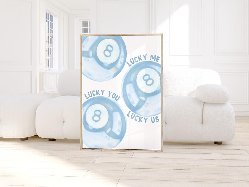May include: A framed print featuring three light blue watercolor-style 8-ball illustrations. The words "LUCKY ME", "LUCKY YOU", and "LUCKY US" are written around the balls. The artwork has a light wooden frame.