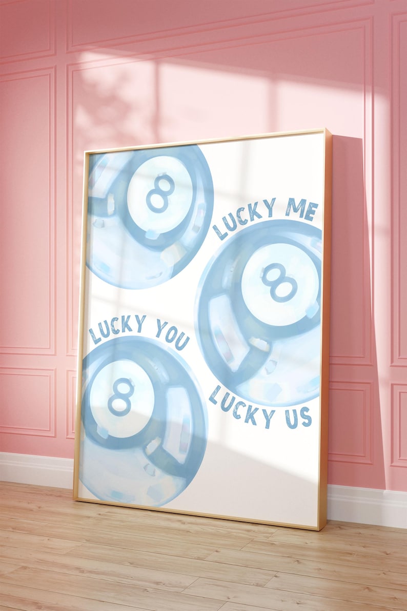 May include: A framed art print featuring three blue watercolor-style eight-ball designs. The words "LUCKY ME", "LUCKY YOU", and "LUCKY US" are written around the balls. The frame is gold, and the background is white.