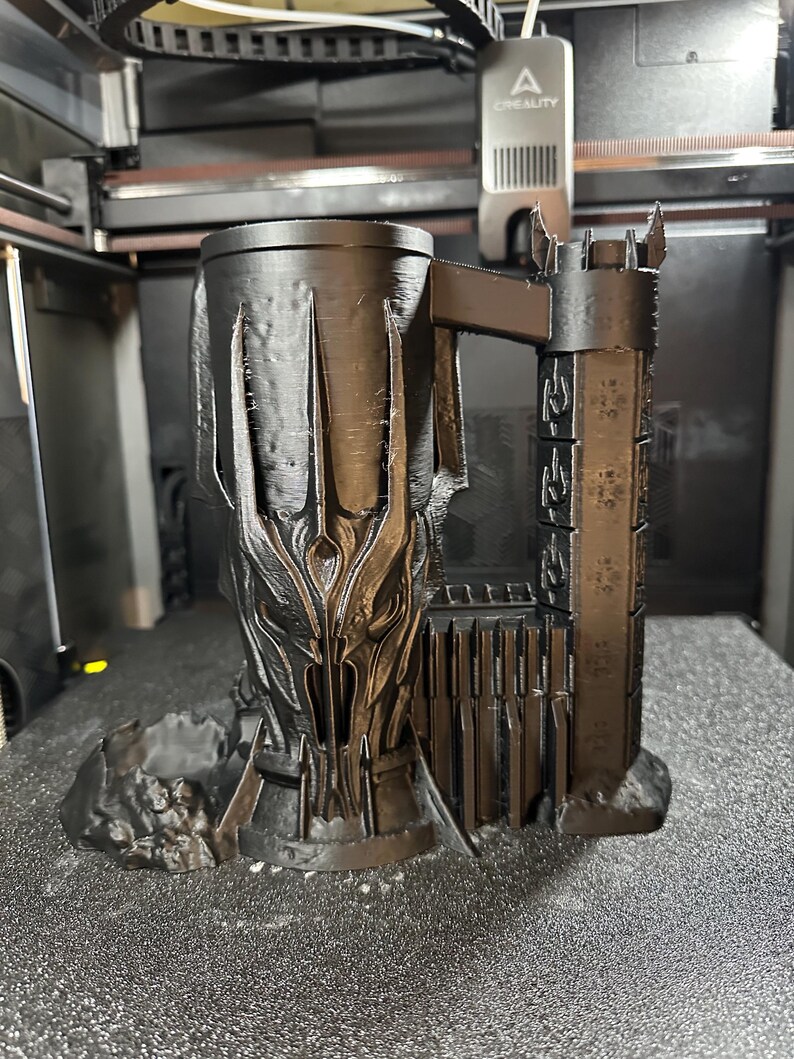 May include: A black 3D printed mug shaped like the tower of Barad-d&ucirc;r from the Lord of the Rings. The mug has a detailed design of the tower and the Eye of Sauron.
