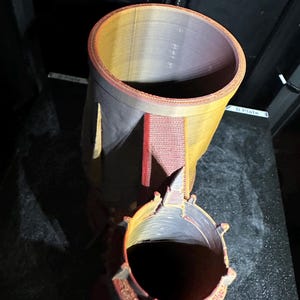 May include: A 3D printed model of a tower with a textured surface. The tower is made of multiple layers of plastic and has a red, orange, and yellow colour scheme. The tower has a cylindrical base and a pointed top.