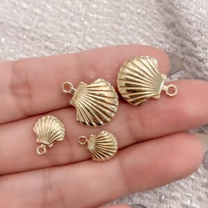 May include: Four gold-coloured seashell charms of varying sizes. The charms have a detailed, textured design and a small loop for attaching to jewellery.