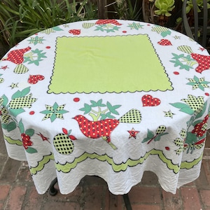May include: A round white tablecloth featuring a large central lime green square with a scalloped edge. The fabric is decorated with a repeating pattern of red birds with yellow polka dots, green checkered fruits, red hearts, and green star shapes.