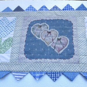 May include: A handmade quilt with a central blue square featuring three embroidered hearts with the words "love", "family", and "friends". The quilt has a patchwork design with various blue and white patterns, including triangles and floral prints.
