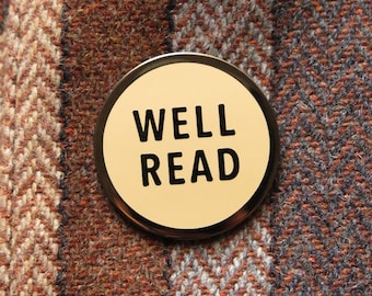 May include: A round, cream-coloured button with black text that reads "WELL READ" on a brown and white patterned fabric.