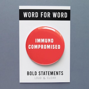 May include: Red button with the text "Immuno Compromised" in white. The button is on a white card with the text "Word for Word" in black at the top and "Bold Statements Loud & Clear" in black at the bottom.