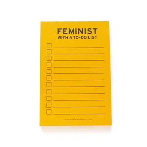 A vertical rectangle goldenrod notepad that reads FEMINIST WITH A TO-DO LIST at the top, with lines f& check boxes for list making.