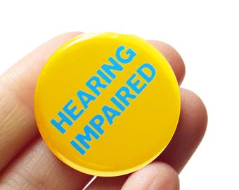 May include: A yellow button with the text "HEARING IMPAIRED" in blue lettering.
