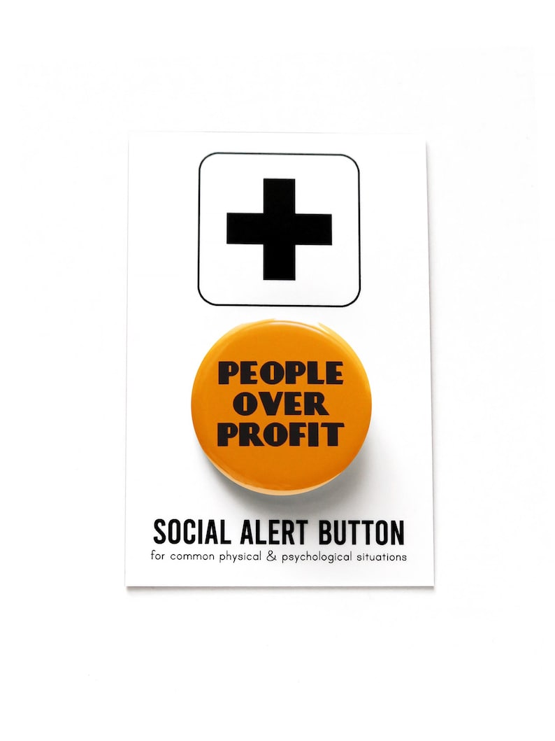 A yellow-orange round pinback button that reads PEOPLE OVER PROFIT in a black art deco font. Button is on a Social Alert Button backing card.