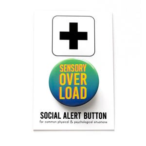 A round green to blue ombre pinback button that reads SENSORY OVERLOAD in yellow text with a pink drop shadow. Badge is on a branded Social Alert Button backing card.