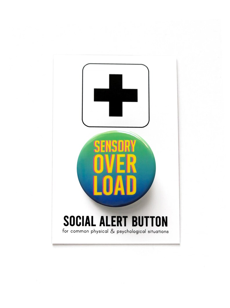 A round green to blue ombre pinback button that reads SENSORY OVERLOAD in yellow text with a pink drop shadow. Badge is on a branded Social Alert Button backing card.