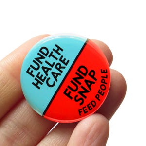 May include: A round button with a diagonal split design. The top half is light blue with the words "FUND HEALTH CARE" in black. The bottom half is red with the words "FUND SNAP FEED PEOPLE" in black.